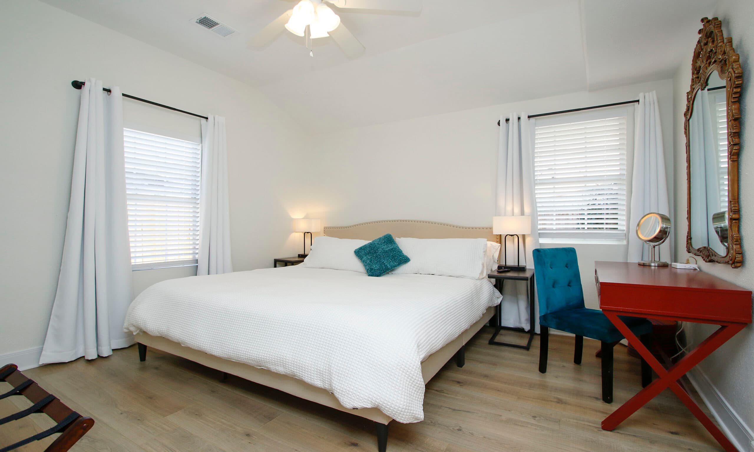 Master bedroom with king bed, teal accents, ornate gold mirror, and red desk