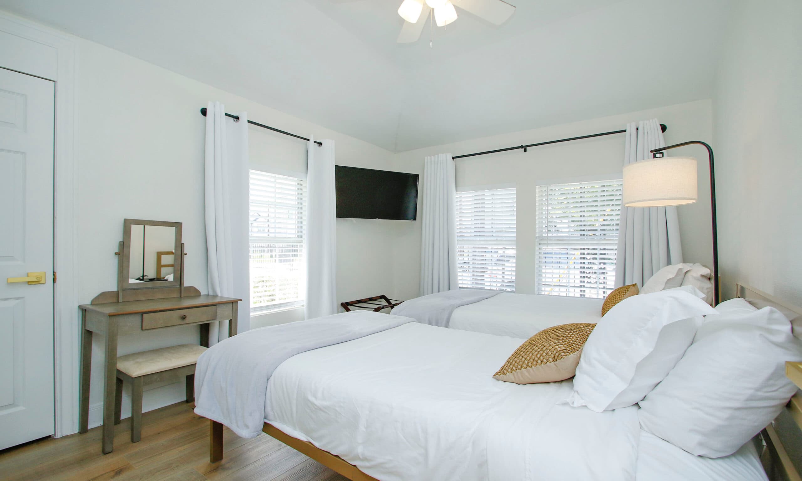 Second bedroom with twin beds, vanity desk, and wall-mounted smart TV